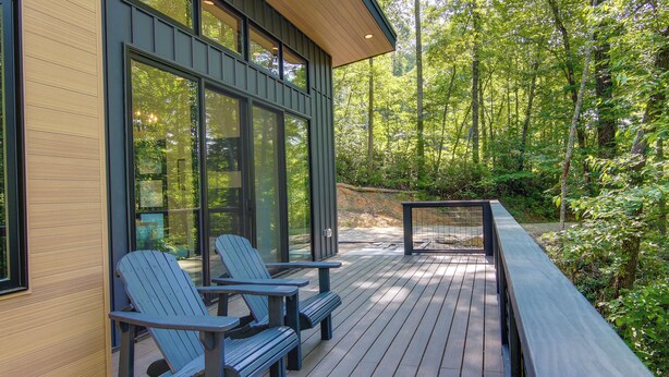 A wooden deck with Adirondack chairs, large windows, and a view of a forested area. - Modern Cabin w/ Hot Tub & Fire Pit in Fairview! (Fairview)