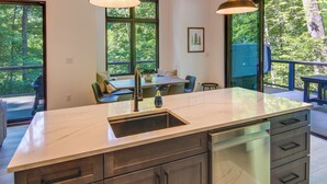 A modern kitchen with a marble countertop, stainless steel appliances, and large windows offering a view of the outdoors. - Modern Cabin w/ Hot Tub & Fire Pit in Fairview! (Fairview)