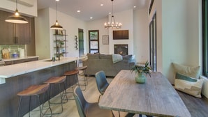A modern kitchen with bar stools, a dining table, and a cozy seating area with a sofa and cushions. - Modern Cabin w/ Hot Tub & Fire Pit in Fairview! (Fairview)