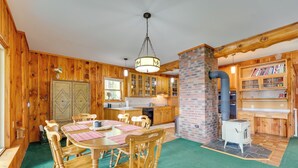 A wooden interior with a dining table, chairs, a chandelier, and a brick fireplace. - Porch & Views: Queensbury 'three Family Lakehouse' (Lake George)