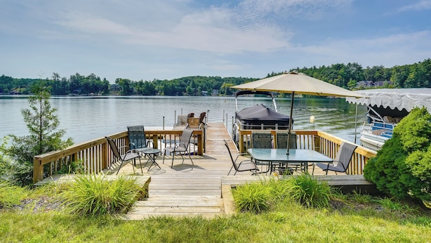 A wooden deck with outdoor furniture overlooking a lake, a covered seating area, and a boat docked nearby. - Porch & Views: Queensbury 'three Family Lakehouse' (Lake George)
