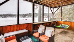 A cozy room with large windows, a wooden ceiling, wicker furniture, and a swing chair. - Porch & Views: Queensbury 'three Family Lakehouse' (Lake George)