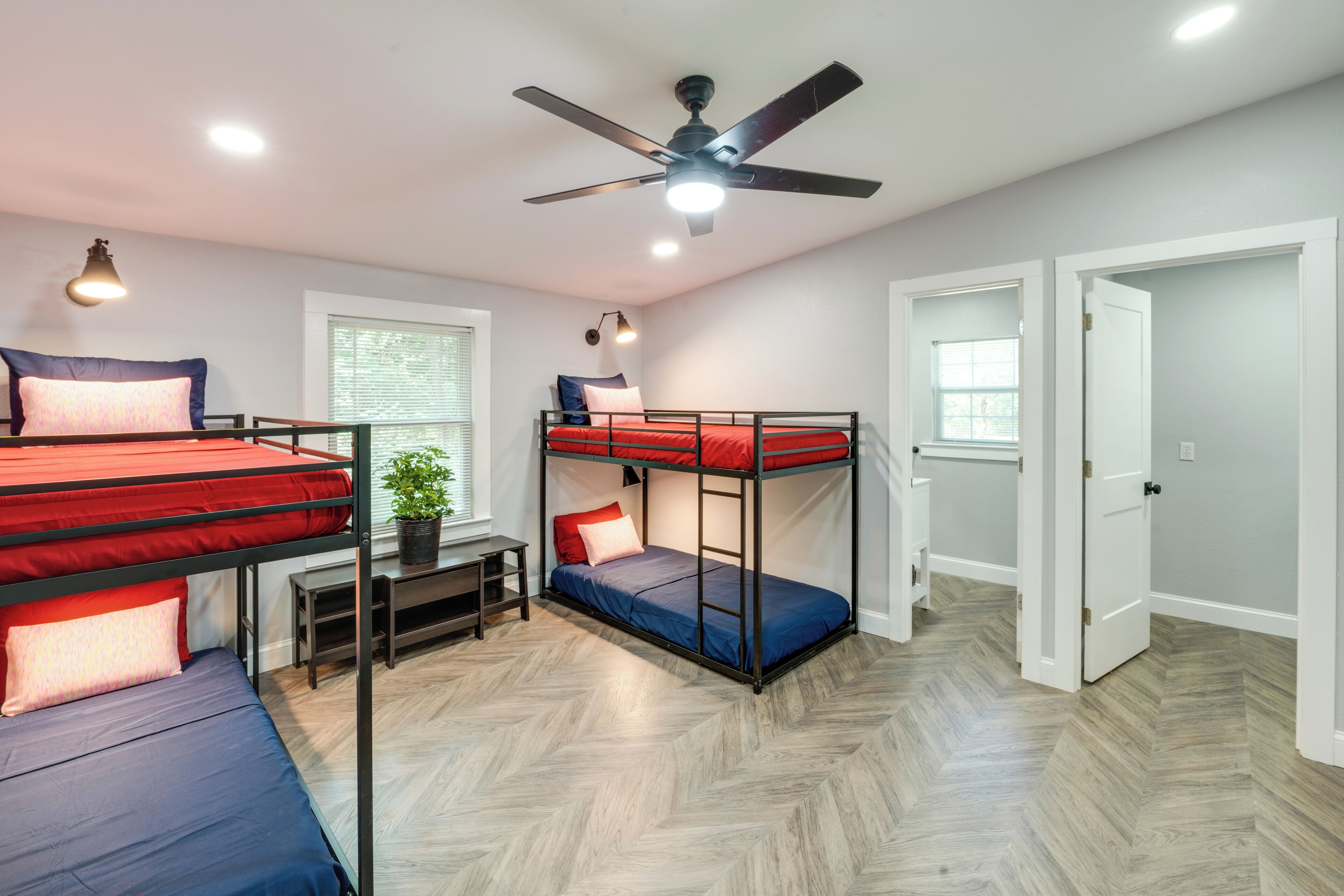 A dormitory room with bunk beds, a ceiling fan, a desk, and a potted plant.