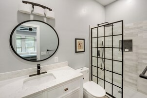 Un baño moderno con un espejo redondo, un lavabo de mármol blanco, un inodoro y una ducha con mampara de vidrio.