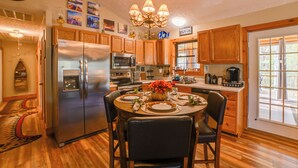 A modern kitchen with wooden cabinets, stainless steel appliances, and a dining area set for four. - Cadiz Vacation Home w/ Deck: Walk to Lake Barkley (Cadiz)