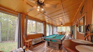 A pool table in a room with wooden floors and large windows, a ceiling fan, and a view of the outdoors. - Cadiz Vacation Home w/ Deck: Walk to Lake Barkley (Cadiz)