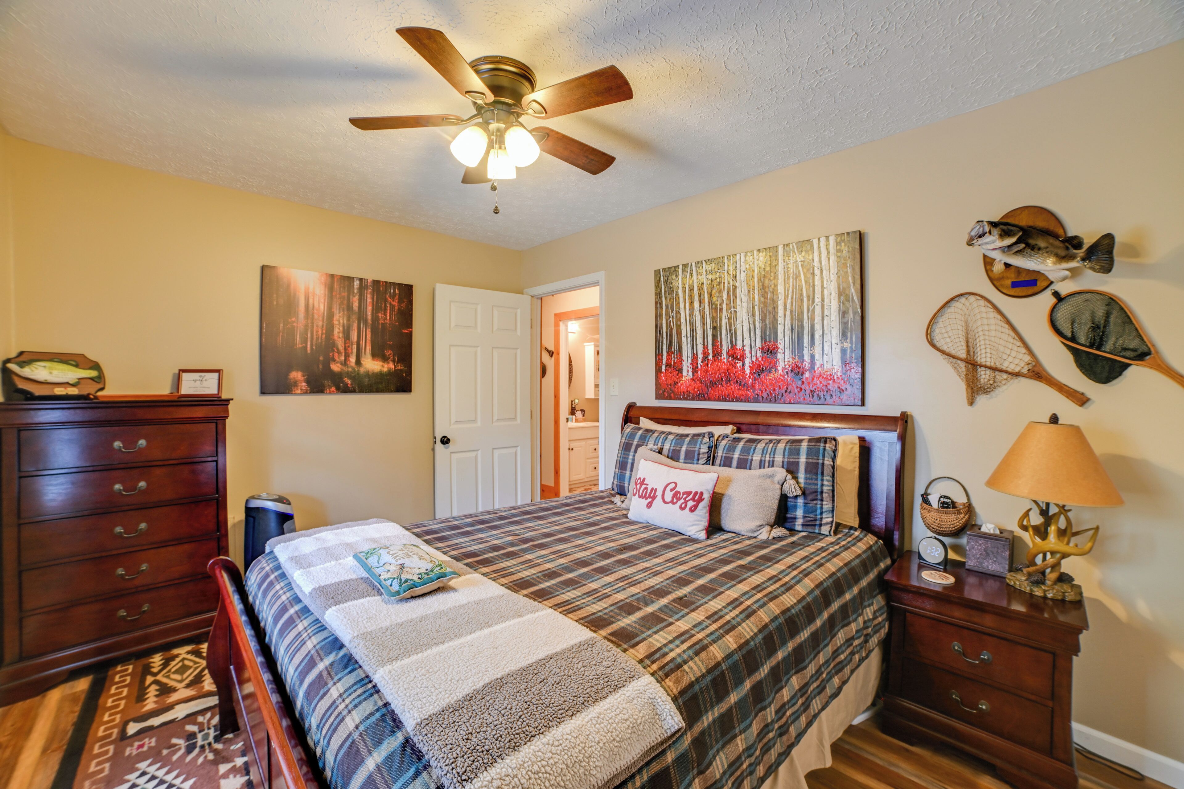 A bedroom with a bed, a ceiling fan, a nightstand, a dresser, and wall decorations.