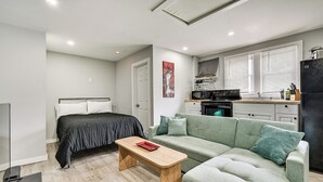 Een compacte woonruimte met een bed, een groene bank, een houten salontafel, en een keukenhoek met een magnetron, fornuis en koelkast.