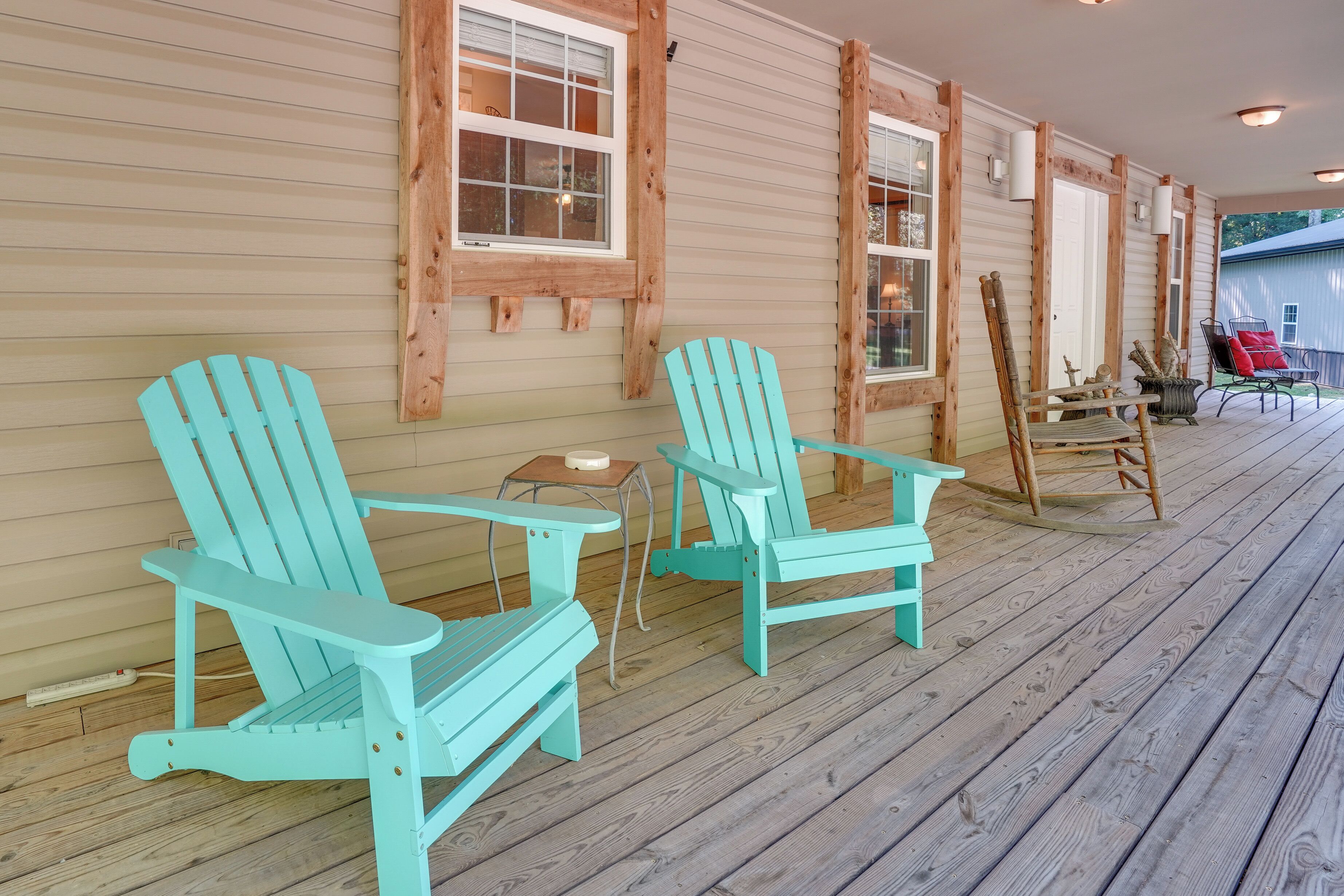 Una terraza de madera con dos sillas Adirondack turquesa y una mesita.