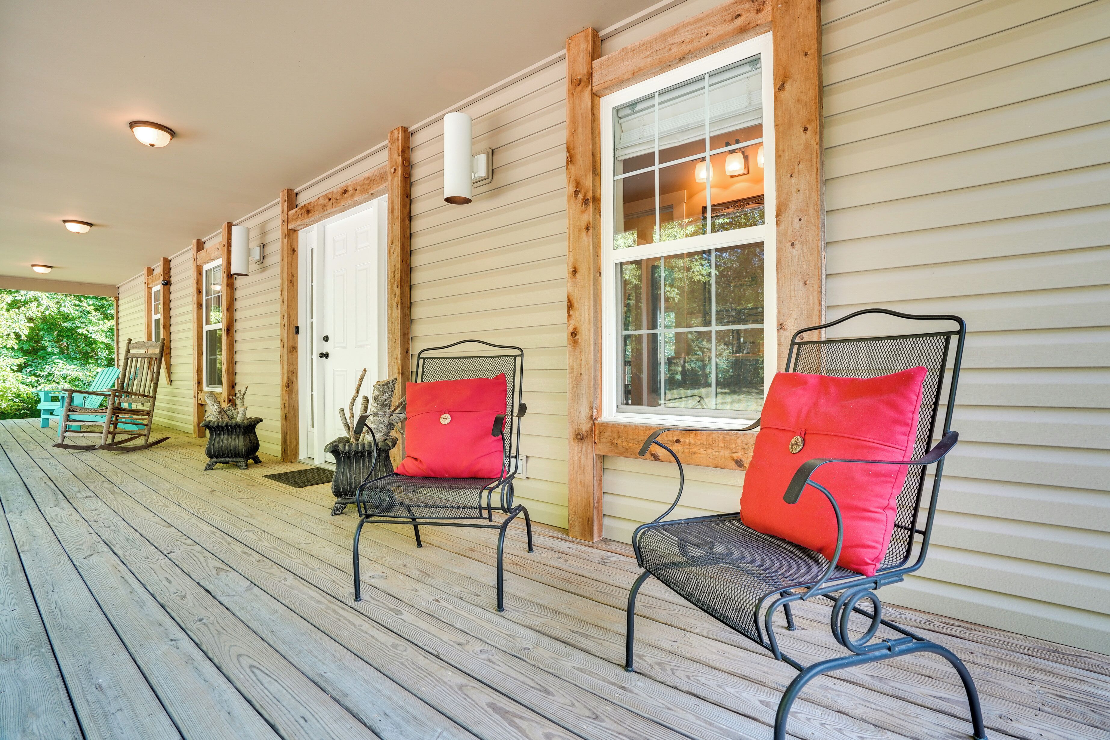 A covered porch with wooden railings, two metal chairs with red cushions, and a rocking chair.