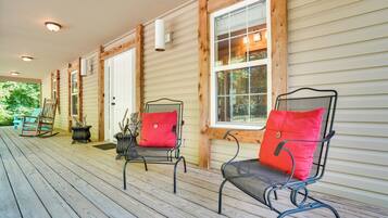 A covered porch with wooden railings, two metal chairs with red cushions, and a rocking chair.