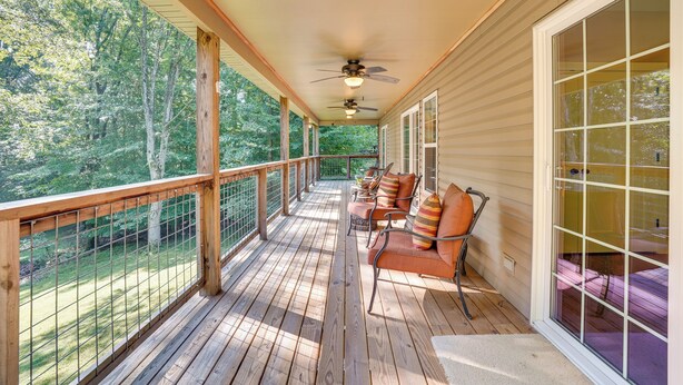 Une terrasse en bois avec une rambarde, un ventilateur de plafond et un espace salon agrémenté de coussins.