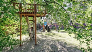 Un parque infantil con una estructura de madera para escalar, un tobogán y columpios.