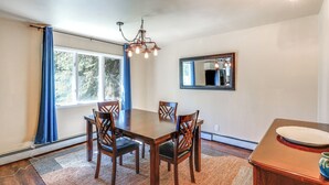 Un comedor con una mesa y sillas de madera, una araña, un espejo y una ventana con cortinas.