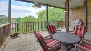 A covered deck with wicker furniture and a table, overlooking a forested area. - Lake Ouachita Vacation Rental w/ Community Pool (Mount Ida)