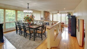 A spacious dining area with a wooden table and chairs, a chandelier, and a view of the outdoors through large windows. - Lake Ouachita Vacation Rental w/ Community Pool (Mount Ida)