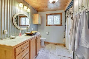 A bathroom with a wooden vanity, a round mirror, a sink with a soap dispenser, a toilet, and a shower area with towels. - Minnesota Cabin w/ Deck & Private Beach (Merrifield)