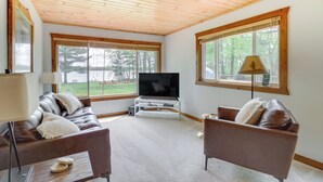 A living room with a wooden ceiling, large windows, a TV, leather sofas, and a lamp. - Minnesota Cabin w/ Deck & Private Beach (Merrifield)