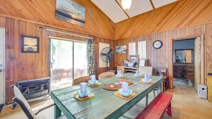 Une salle à manger en bois avec une table dressée pour six personnes, une cheminée et une horloge au mur.