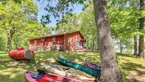 Un chalet rustique, doté de fondations en pierre et d’un revêtement extérieur en bois, entouré d’une végétation luxuriante et bordé d’un lac paisible.