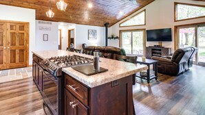 Una cocina amplia con una isla grande, armarios de madera y una estufa empotrada. Hay una zona de estar con un sofá y una televisión.