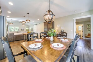 A dining room with a wooden table set for four, surrounded by chairs, a chandelier, and a vase with flowers.