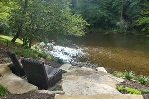 A stone patio with wicker chairs overlooking a river.