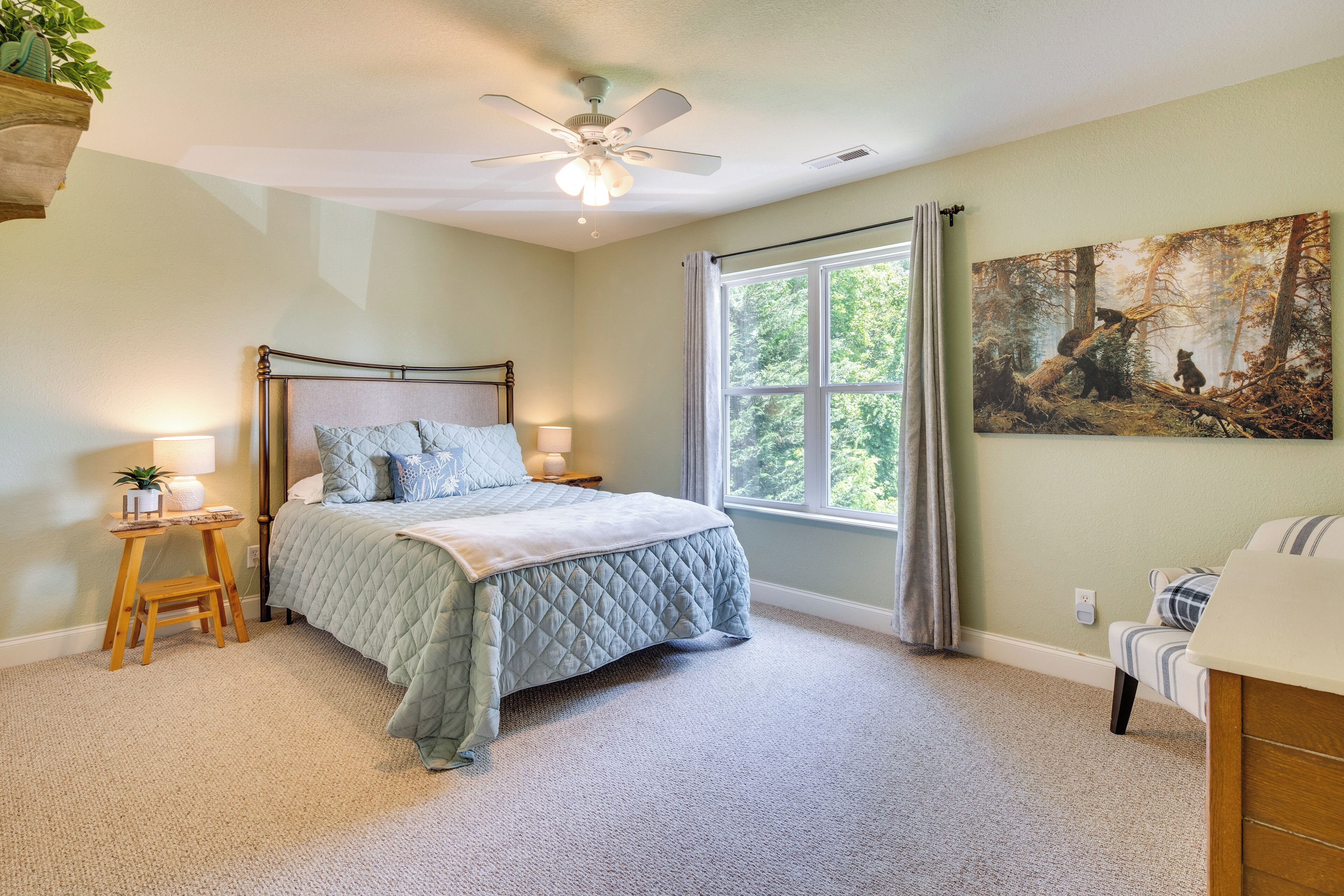A bedroom with a bed, bedside lamps, a window with curtains, a ceiling fan, and a painting on the wall.