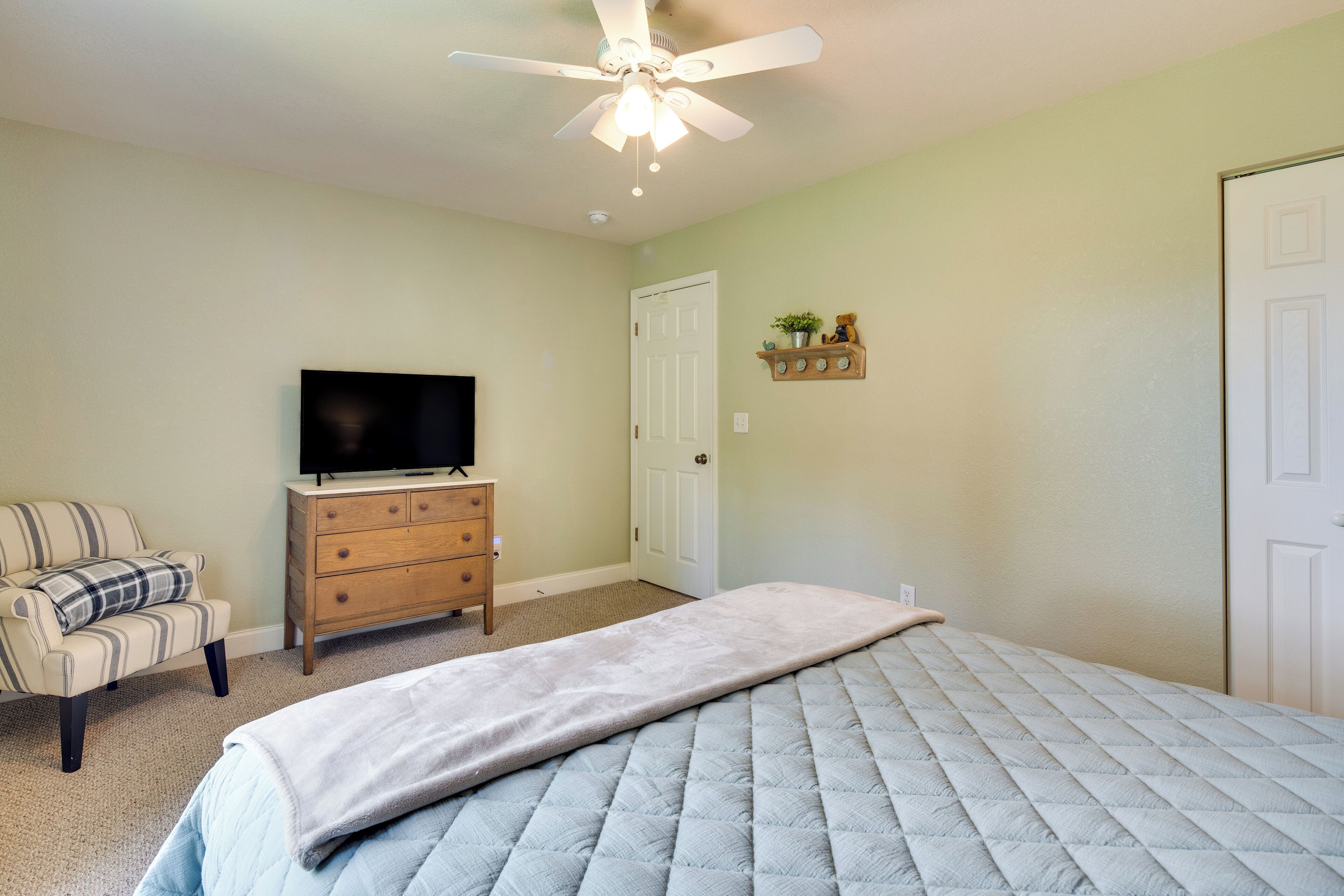 A bedroom with a bed, a television on a dresser, a chair, and a ceiling fan.