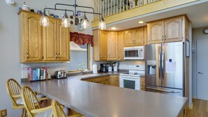 A spacious kitchen with wooden cabinets, a large island, stainless steel appliances, and a dining area with wooden chairs. - Lakefront Vandalia Home w/ Boat Dock & Gas Grill! (Vandalia)
