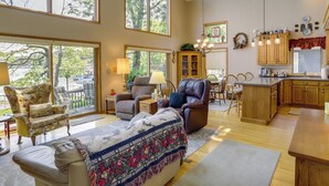 A spacious living room with a large window, a fireplace, and a dining area with wooden furniture. - Lakefront Vandalia Home w/ Boat Dock & Gas Grill! (Vandalia)