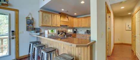 A kitchen with wooden cabinets, a central island with stools, and a view of the outdoors.