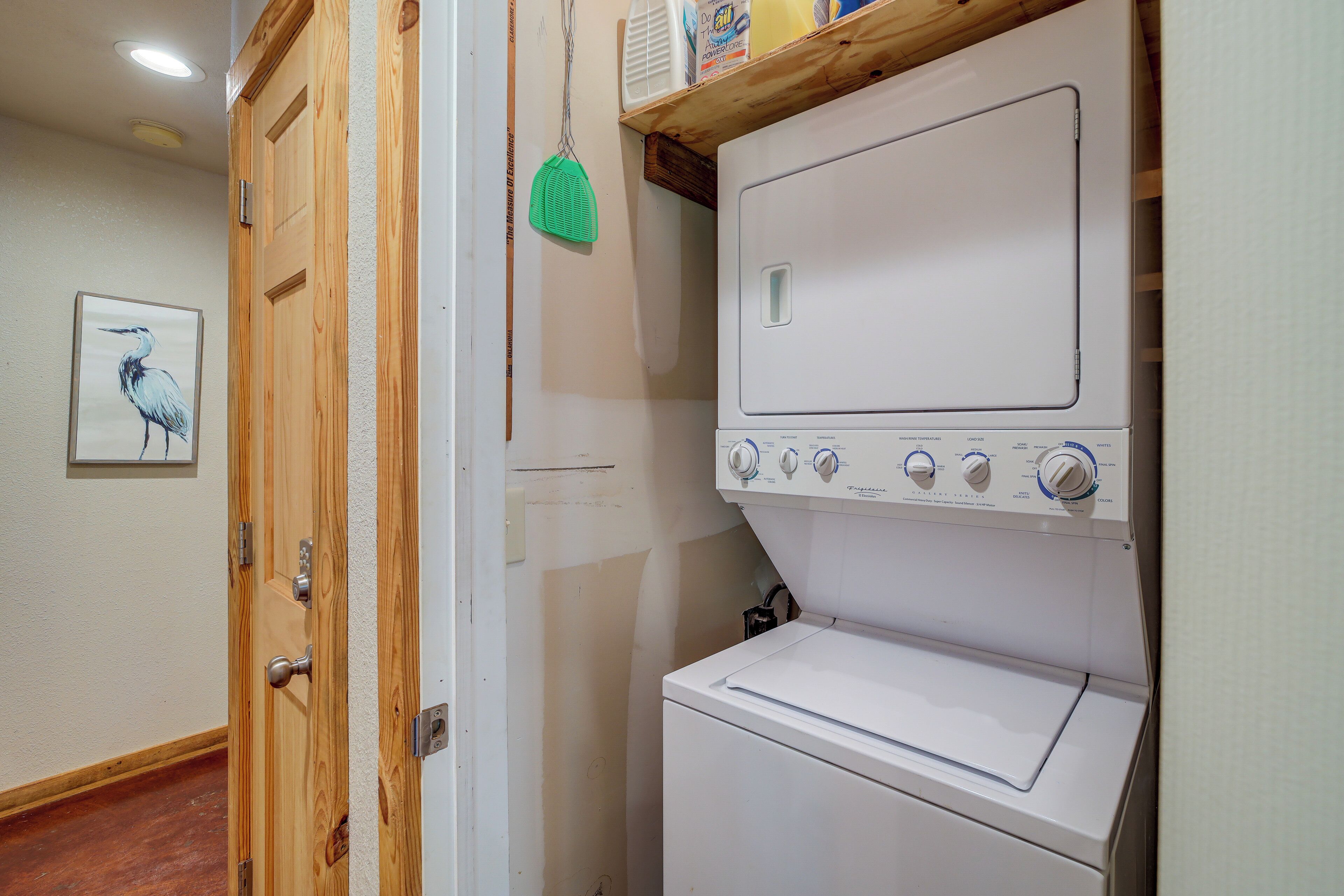 A laundry room with a white washer and dryer, wooden doors, and a framed picture on the wall.