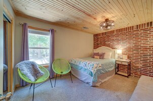 Un dormitorio con pared de ladrillo, una cama con cabecera blanca, una silla verde y una mesita de noche con lámpara.