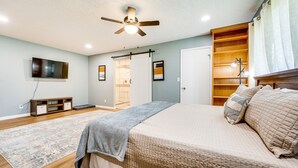 Une chambre à coucher comprenant un lit, un ventilateur de plafond, un téléviseur fixé au mur, une armoire en bois et un placard à portes coulissantes.