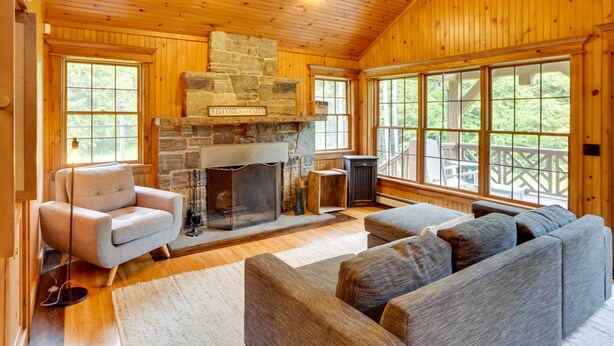 A cabin interior with a stone fireplace, large windows, and a cozy seating area. - Secluded Elka Park Cabin: Hot Tub & Fire Pit! (Tannersville)
