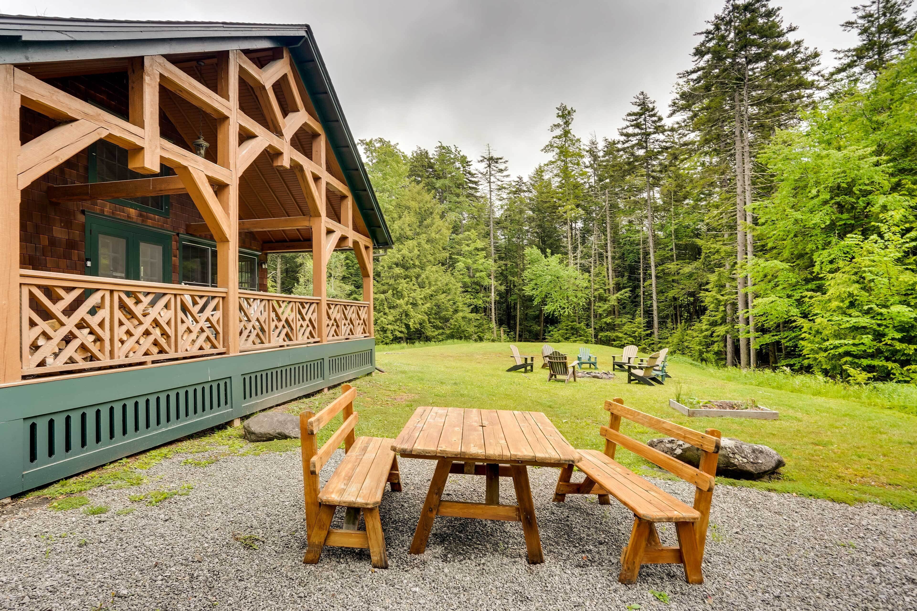 A wooden cabin with a deck, outdoor seating, and a forest backdrop.