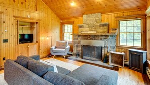 A cozy cabin interior with a stone fireplace, wooden walls, a television, and a gray sofa. - Secluded Elka Park Cabin: Hot Tub & Fire Pit! (Tannersville)
