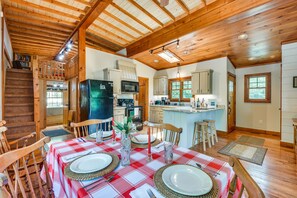 A cozy cabin-style kitchen with wooden beams, a dining area with a checkered tablecloth, and a staircase leading to a loft.