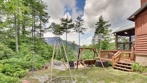 Eine Holzhütte mit einer Veranda, einer Schaukel und einem Hängesessel in bewaldeter Landschaft.