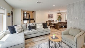 A spacious living room with a grey sectional sofa, a round coffee table, and a grey armchair. A dining area with a wooden table and chairs is visible in the background. - 6 Mi to Hunter Mtn: Winter Retreat w/ Hot Tub! (Tannersville)