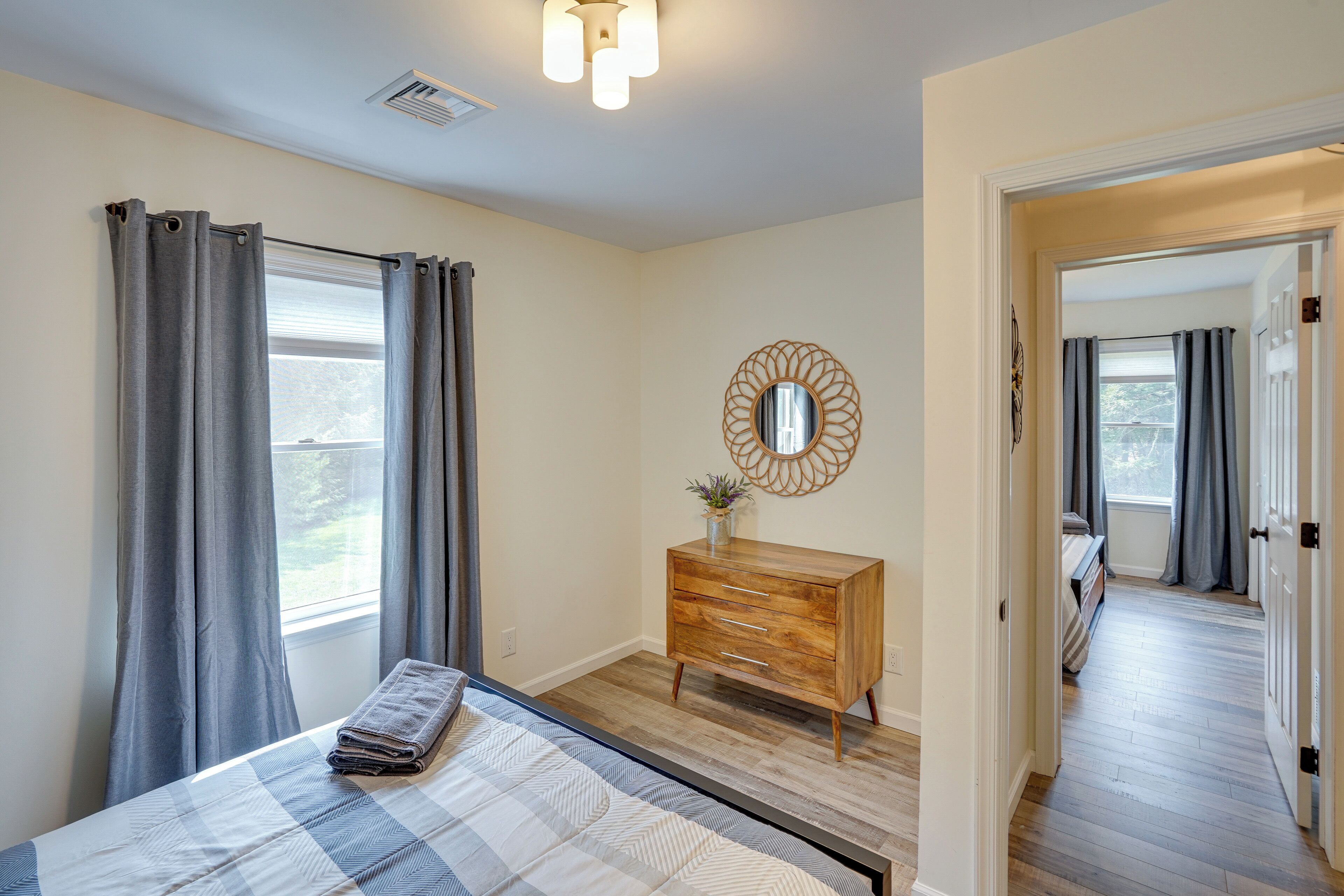 A bedroom with a bed, a wooden dresser, a mirror, and a window with curtains.