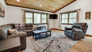 A living room with a wooden ceiling, two windows, a sofa, a chair, a coffee table, and a rug. - Hatfield Vacation Rental w/ Private Hot Tub! (Merrillan)