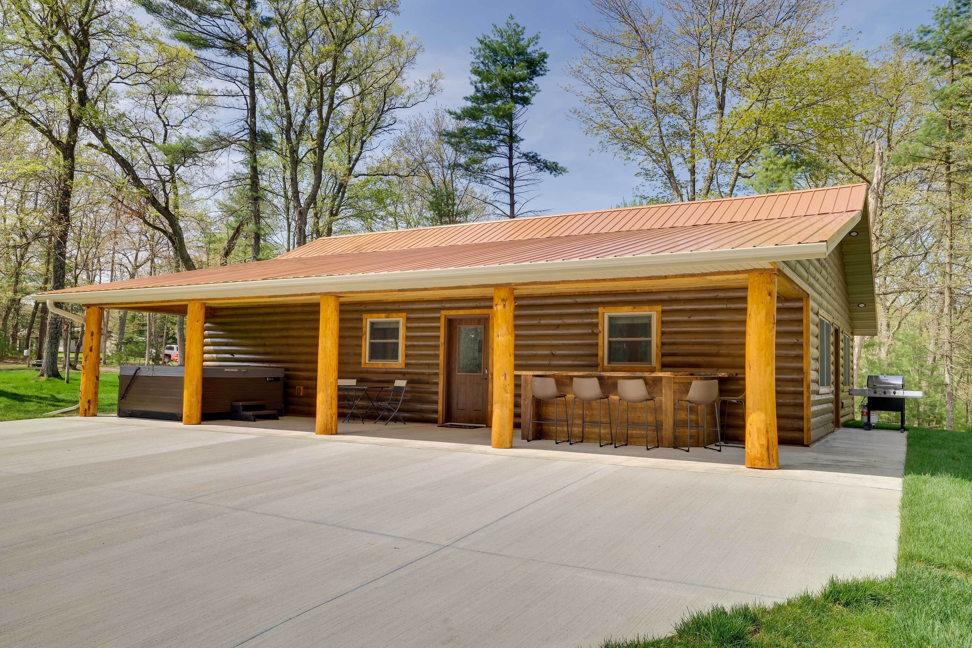 A log cabin with a covered patio, outdoor seating, and a grill area.