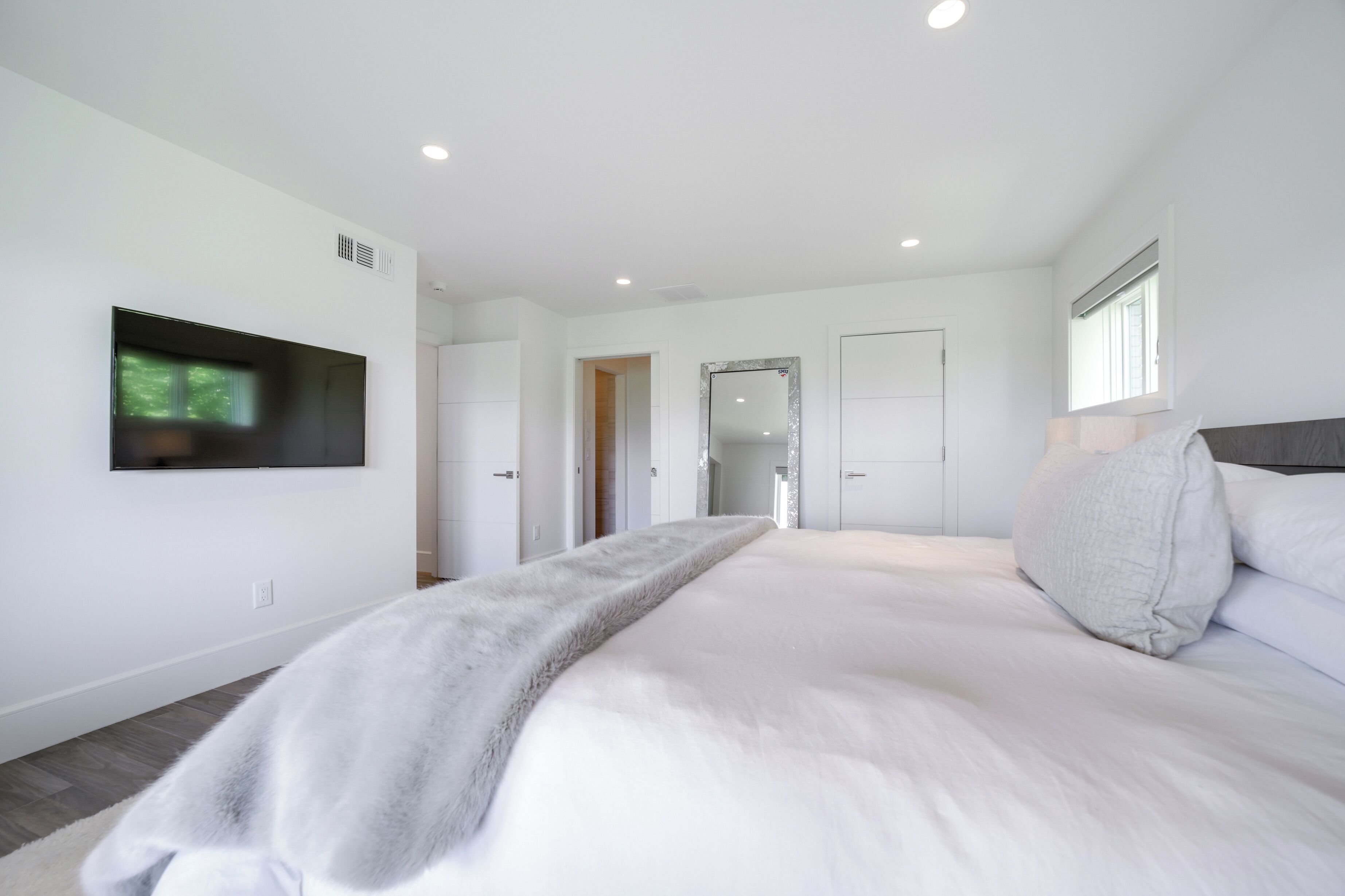 A modern bedroom with a large bed, a flat-screen TV mounted on the wall, and a walk-in closet.