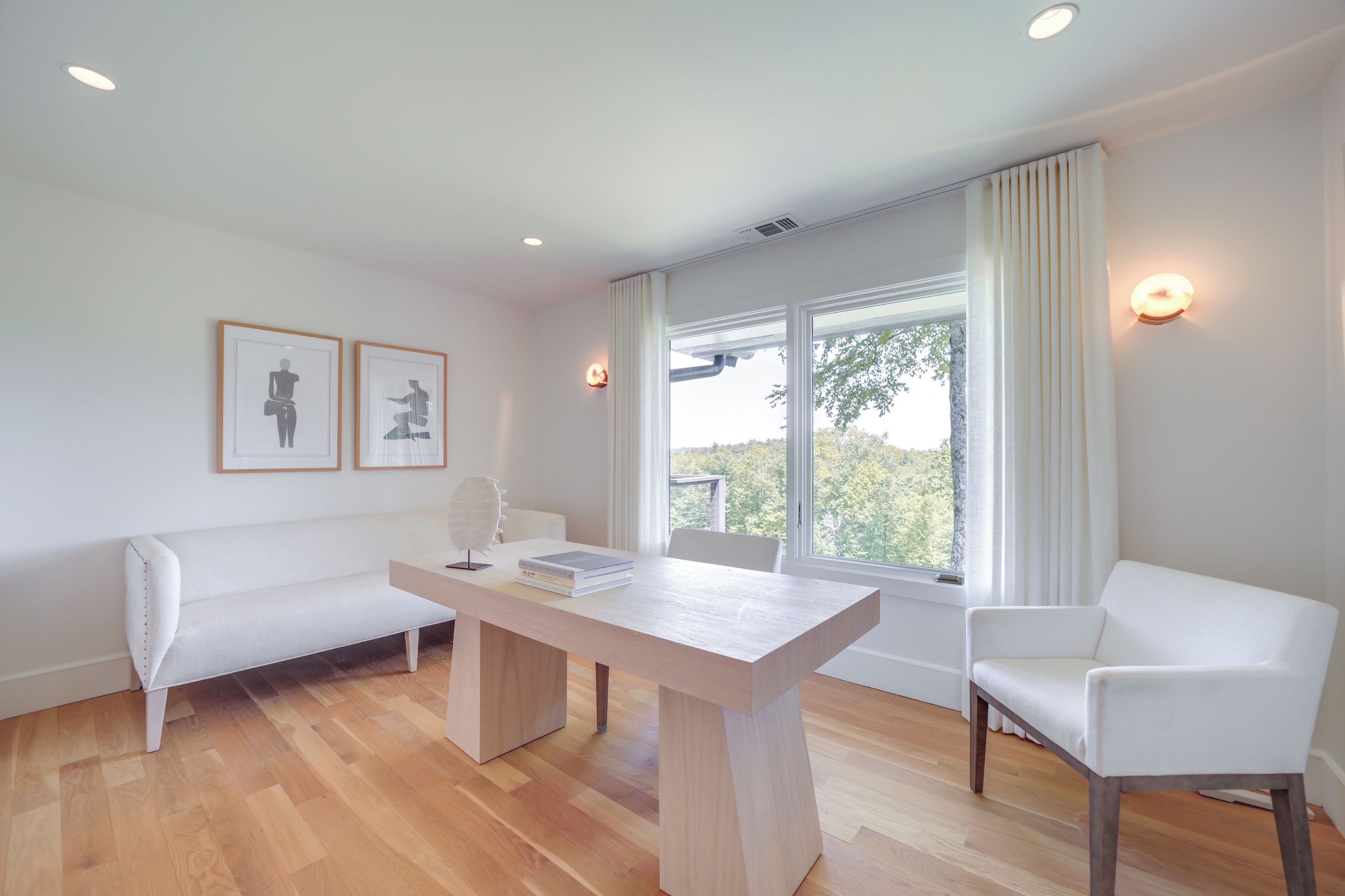 A modern living room with a wooden floor, a white sofa, a white armchair, a wooden coffee table, and two framed pictures on the wall.