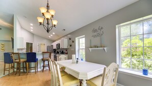A spacious dining area with a white table and chairs, a chandelier, and a kitchen in the background. - Swansboro Vacation Rental, 4 Mi to Hammocks Beach! (Swansboro)