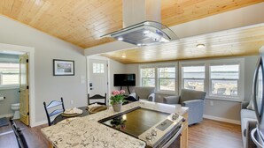 Une cuisine moderne dotée d’un grand îlot central, d’un plafond en bois et de grandes fenêtres donnant sur une plage.