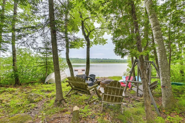 Un espacio de descanso rústico al aire libre con sillas Adirondack y una terraza de madera con vistas a un lago.