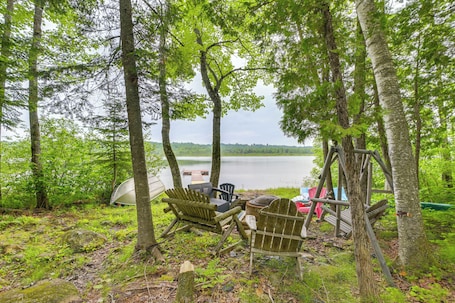 A rustic outdoor seating area with Adirondack chairs and a wooden deck overlooking a lake.